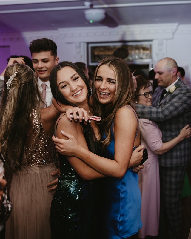 Two wedding guests hugging and laughing on a busy dance floor