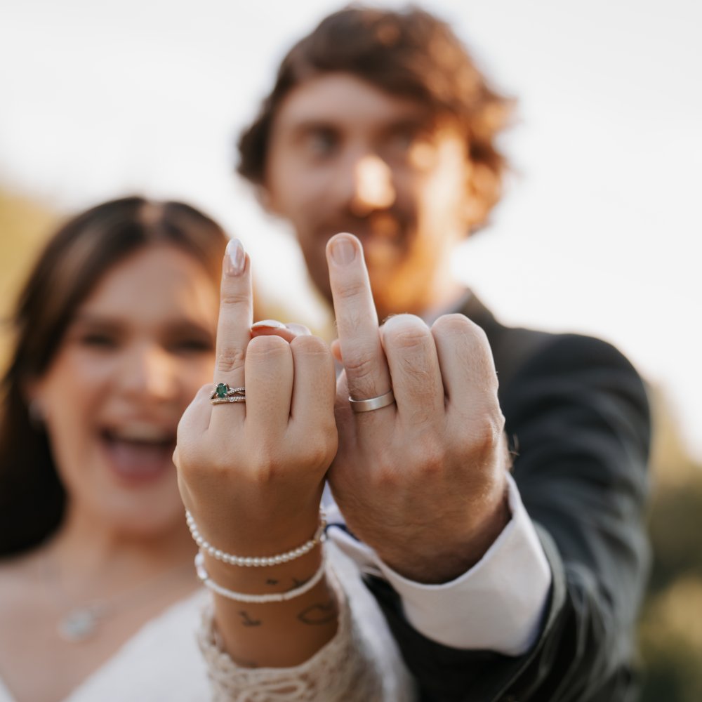 A laughing bride and groom holding up their hands to show off their wedding rings